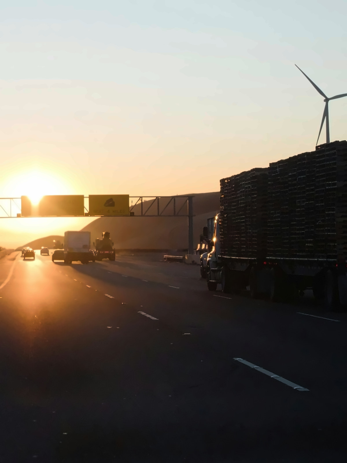 Autoroute au coucher du soleil, sous un portique de signalisation, un camion lourd dans la voie de droite
